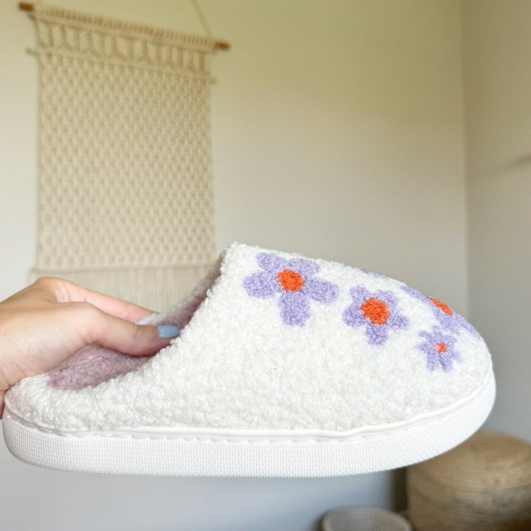 White slipper with floral designs held by a hand against a neutral background