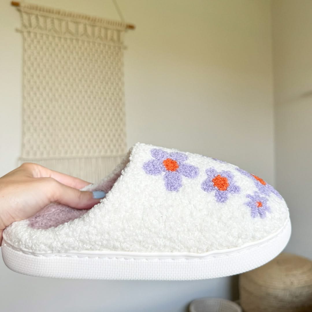 White slipper with floral designs held by a hand against a neutral background