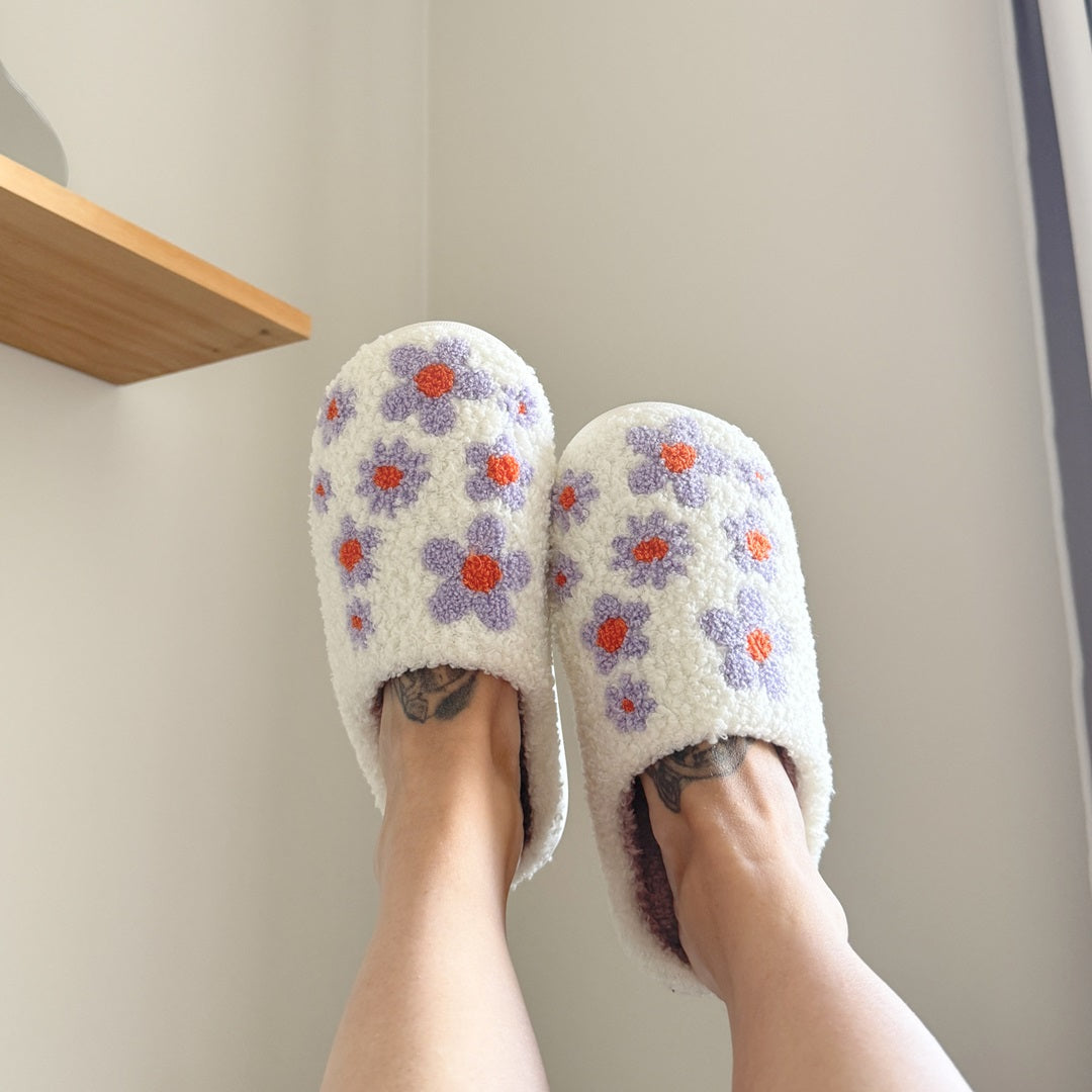 White slippers with floral patterns worn indoors on a neutral background