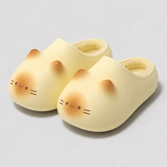 Josh & Tate - PurrPad™ Cozy Cat-Face Slippers - A pair of pale yellow slip-on slippers shaped like a cat's face, with soft peach-colored ear tips, simple black facial features, and a fuzzy cream inner lining, photographed on a light gray studio background.