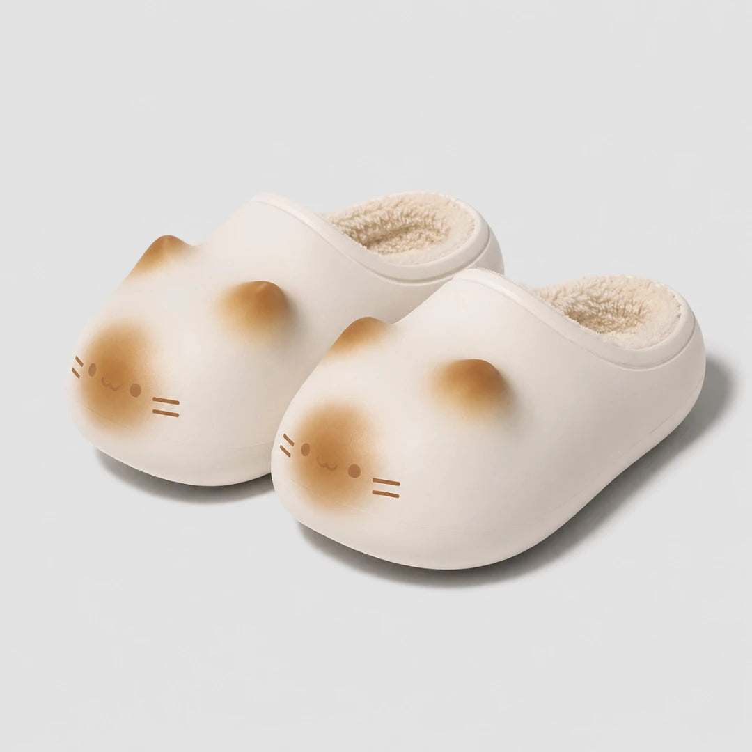 Josh & Tate - PurrPad™ Cozy Cat-Face Slippers - A pair of off-white slip-on slippers shaped like a cat's face, featuring soft tan shading on the cheeks and forehead, with a plush cream lining visible inside, set against a light gray background.