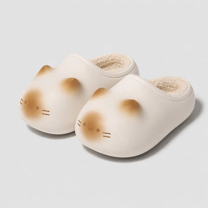 Josh & Tate - PurrPad™ Cozy Cat-Face Slippers - A pair of off-white slip-on slippers shaped like a cat's face, featuring soft tan shading on the cheeks and forehead, with a plush cream lining visible inside, set against a light gray background.