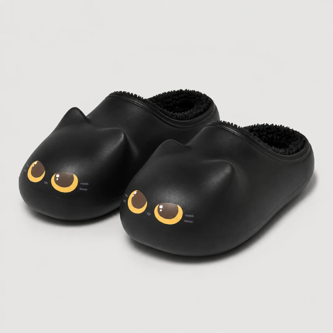 Josh & Tate - PurrPad™ Cozy Cat-Face Slippers - A pair of black slip-on slippers shaped like cat heads, featuring yellow and brown eyes with small white whiskers, shown on a light gray background.