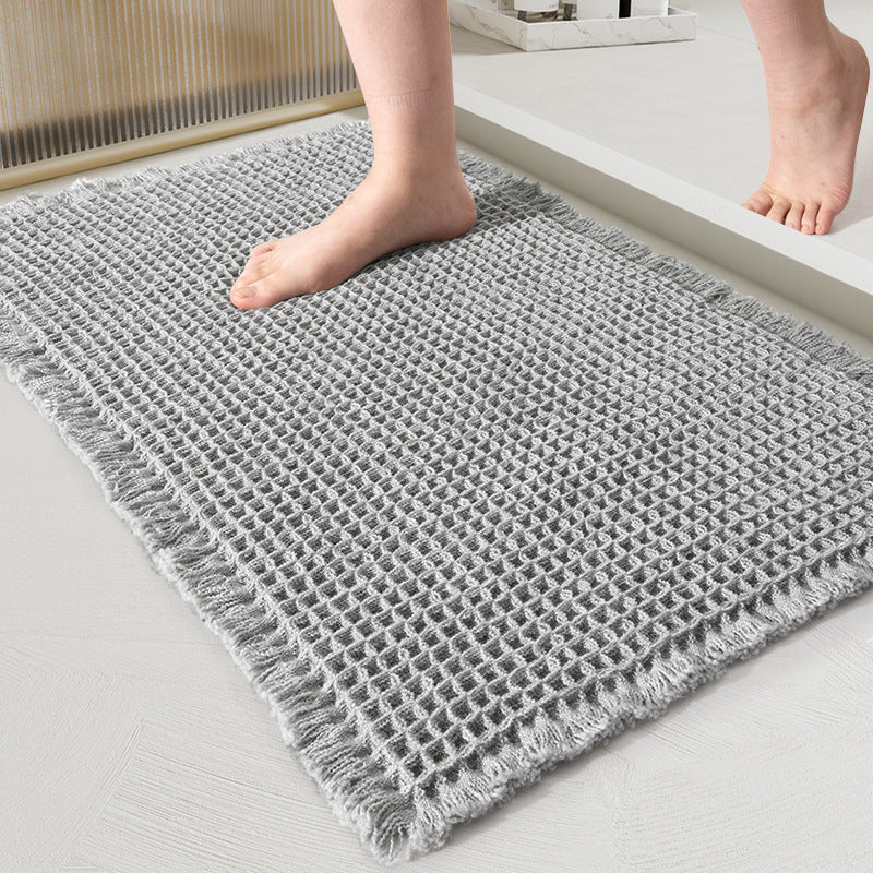 Gray textured rug on a light wooden floor with a person's feet stepping onto it.