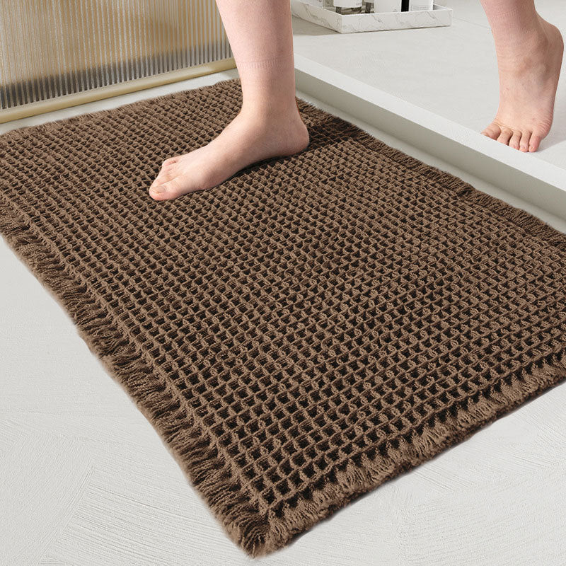 Brown textured bath mat on a light gray floor with feet stepping onto it.
