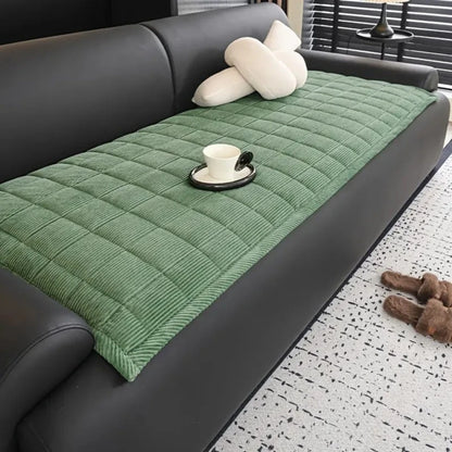 Josh & Tate - QuiltDrape™ Corduroy Sofa Cover - Green quilted sofa cover on a gray sofa with a cup and saucer on a small table.
