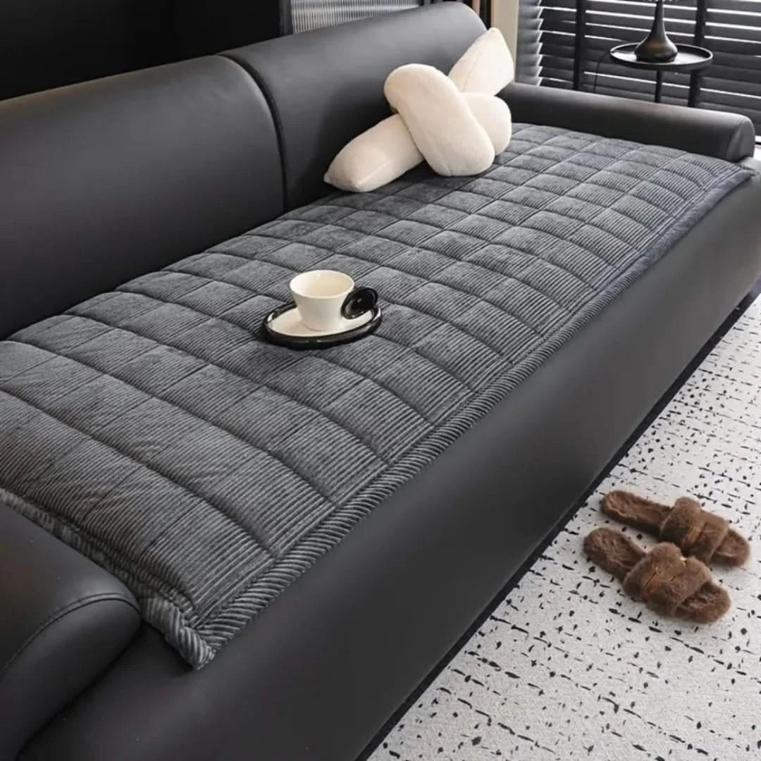 Josh & Tate - QuiltDrape™ Corduroy Sofa Cover - Gray quilted sofa cover on a black sofa with a cup and saucer on a small table.