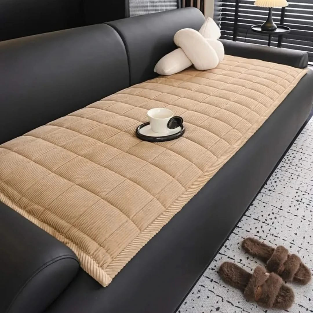 Josh & Tate - QuiltDrape™ Corduroy Sofa Cover - Beige quilted sofa cover on a black sofa with a cup and saucer on a small table.