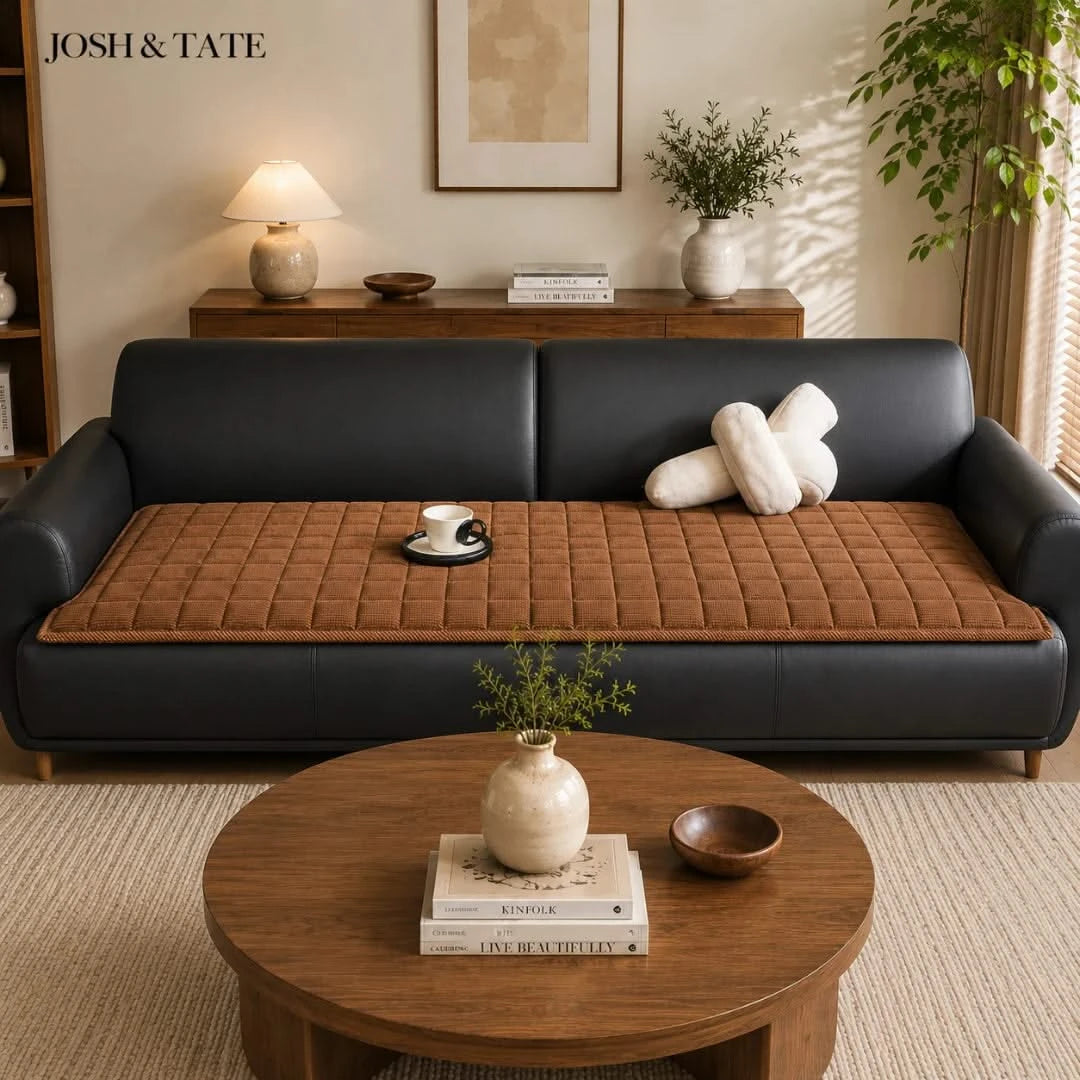 Josh & Tate - QuiltDrape™ Corduroy Sofa Cover - Living room with a black sofa and brown cushion, a wooden coffee table with decor items, and 'JOSH & TATE' branding.