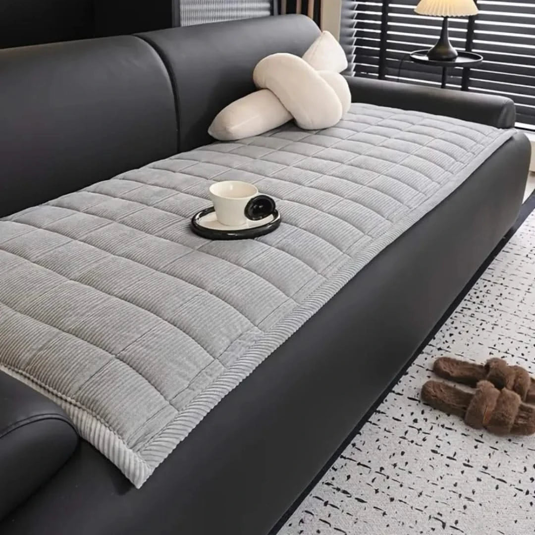 Josh & Tate - QuiltDrape™ Corduroy Sofa Cover - Gray quilted sofa cover on a black sofa with a cup and saucer on a small table.