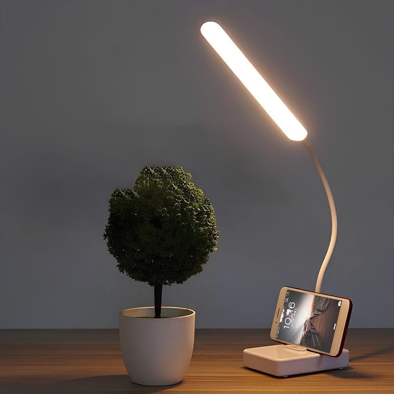 Table lamp with phone charging stand next to a potted plant on a wooden surface.