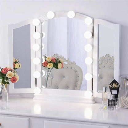 Tri-fold vanity mirror with lights on a white dresser with decorative items.