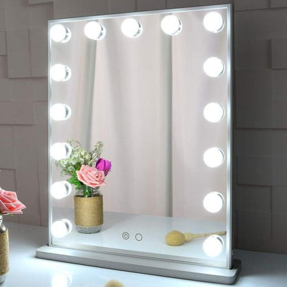 Makeup mirror with lights on a white surface with flowers and a brush.