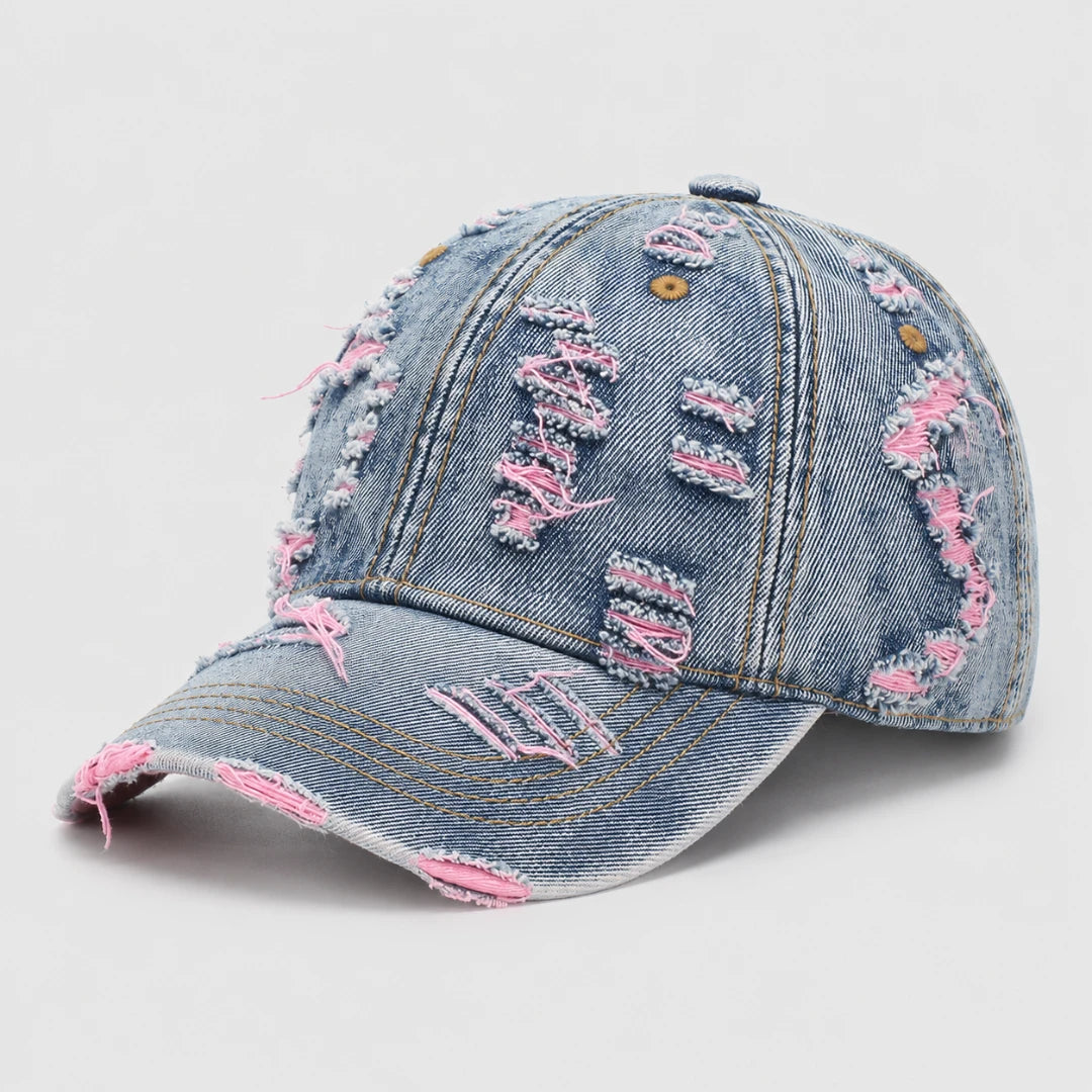Josh & Tate - RaggedRow™ Distressed Denim Cap - A distressed light blue denim baseball cap with frayed details and pink accents, photographed on a light gray background.