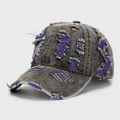 Josh & Tate - RaggedRow™ Distressed Denim Cap - A distressed baseball cap made of gray denim with ripped details showing a vibrant purple lining, photographed on a light gray background.