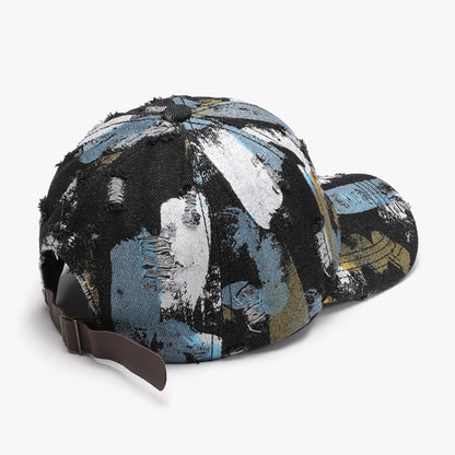 Josh & Tate - RawCanvas™ Painted Baseball Cap - A distressed baseball cap featuring an abstract paint-splatter pattern in black, light blue, white, and gold, with a brown adjustable strap.