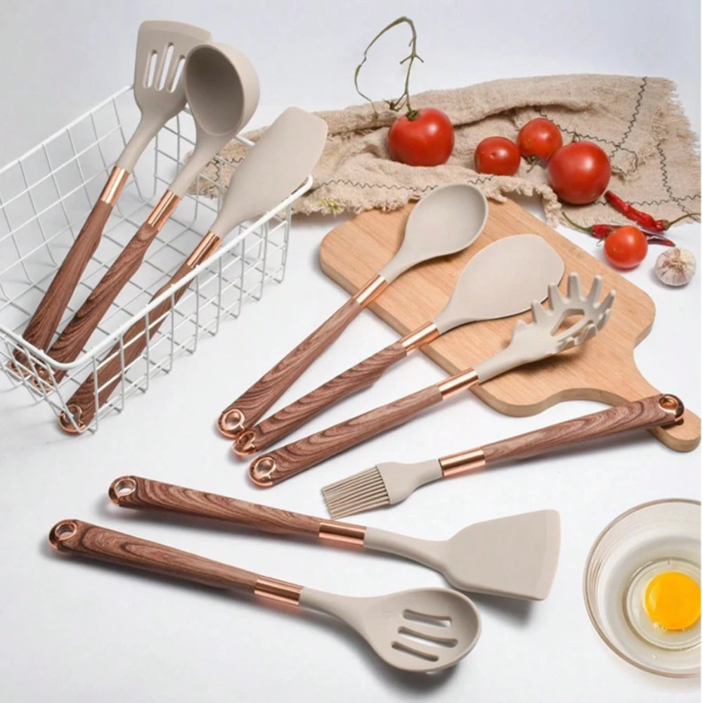 Set of kitchen utensils with wooden and rose gold handles on a white surface.
