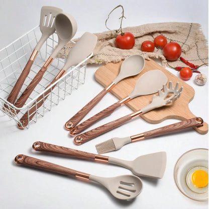 Set of kitchen utensils with wooden and rose gold handles on a white surface.