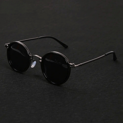 Round sunglasses with black lenses and thin metal frame on a dark background