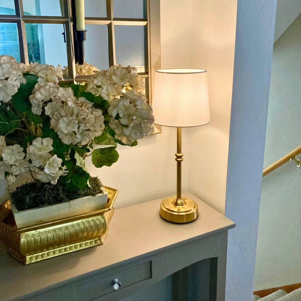 Decorative table with a gold lamp and white flowers in a room with a mirror and light blue wall.