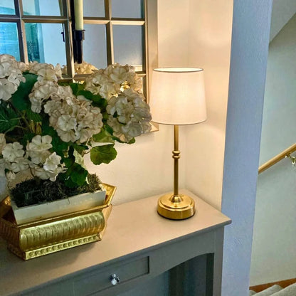 Decorative table with a gold lamp and white flowers in a room with a mirror and light blue wall.