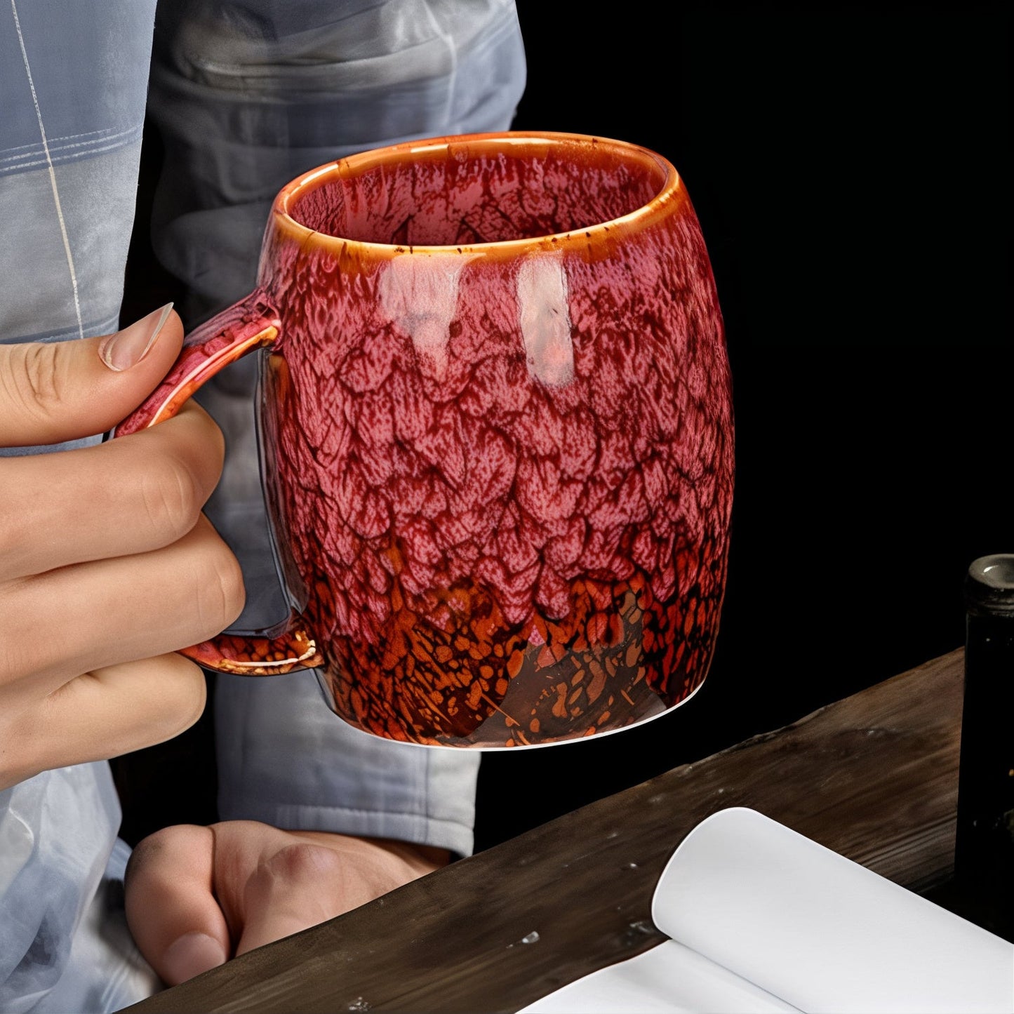 Person holding a red ceramic mug with a textured surface on a wooden table.
