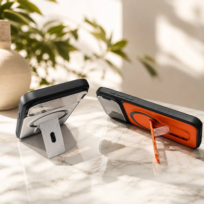 Josh & Tate - RingArmor™ MagSafe iPhone Case - Two MagSafe-compatible phone cases displayed on a marble surface in a sunlit room. One case is black with a clear magnetic ring and a white stand, and the other is black with an orange magnetic ring and a clear stand.