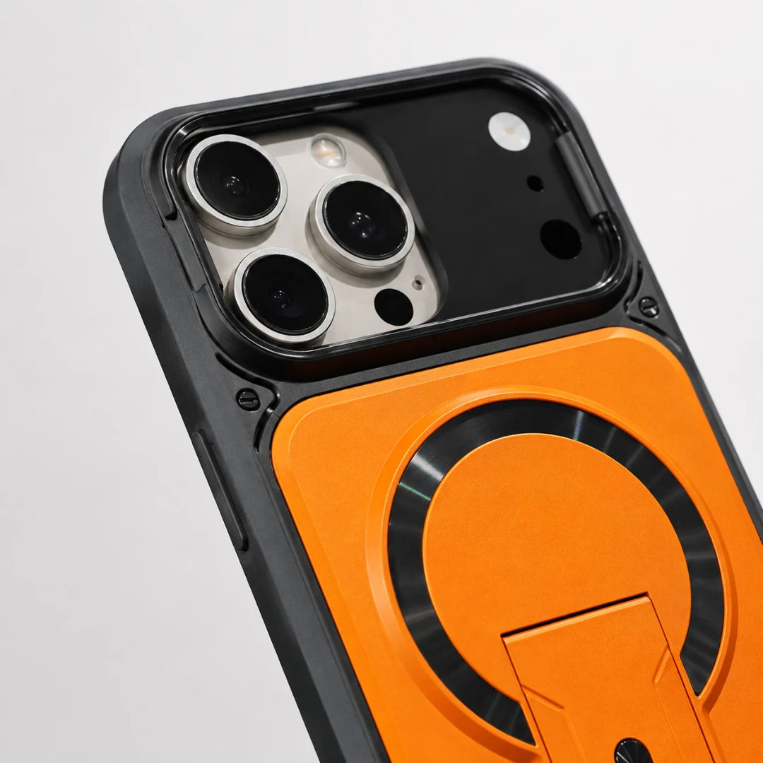 Josh & Tate - RingArmor™ MagSafe iPhone Case - Close-up of a smartphone case with a black outer frame and a bright orange back panel featuring a circular MagSafe-style ring and kickstand detail, shown on a light gray background.