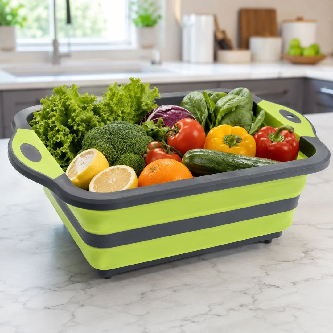 Josh & Tate - RinseFold™ Cutting & Drain Board - A lime green and dark gray collapsible silicone salad spinner basket filled with fresh vegetables, including lettuce, broccoli, tomatoes, peppers, cucumber, and lemons, set on a white marble kitchen countertop.