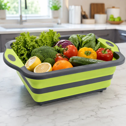 Josh & Tate - RinseFold™ Cutting & Drain Board - A lime green and dark gray collapsible silicone salad spinner basket filled with fresh vegetables, including lettuce, broccoli, tomatoes, peppers, cucumber, and lemons, set on a white marble kitchen countertop.