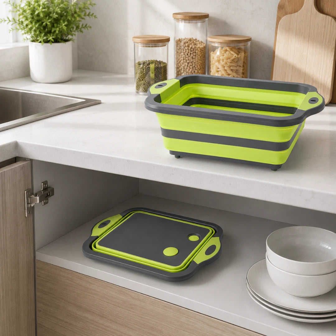 Josh & Tate - RinseFold™ Cutting & Drain Board - A bright lime green and dark gray collapsible rectangular dish rack and matching cutting board set displayed on a kitchen countertop, with one set open on the counter and another folded inside a cabinet below. The scene includes a sink, glass jars with wooden lids, a potted plant, and stacked white bowls and plates.