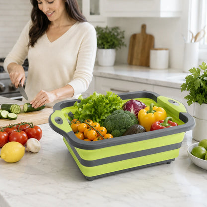 Josh & Tate - RinseFold™ Cutting & Drain Board - A woman in a cream sweater is shown in a bright kitchen preparing food, with a collapsible lime green and gray plastic basket filled with fresh vegetables on the counter in the foreground.