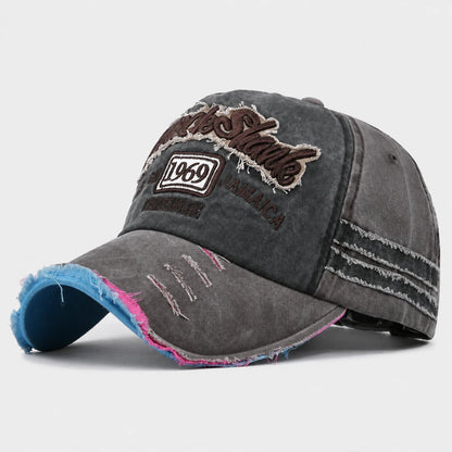 Josh & Tate - RockShank™ 1969 Baseball Cap - A distressed dark gray washed baseball cap with embroidered 'The Stand' and '1969' patches on the front, featuring frayed details, a blue and pink lining on the brim, and white stitched stripes on the side panels.