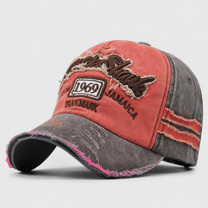 Josh & Tate - RockShank™ 1969 Baseball Cap - A distressed baseball cap with a washed coral-red front panel and brim, dark gray sides, and embroidered text including 'Jamaica', '1969', and 'Trademark'.