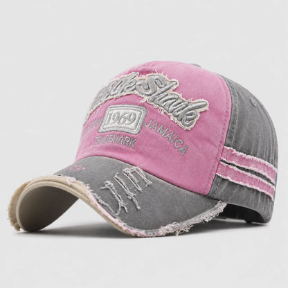 Josh & Tate - RockShank™ 1969 Baseball Cap - A distressed baseball cap with a pink front panel and a gray washed denim-like back and brim. The front features embroidered text reading 'Jamaica' and '1969' with a small 'Trademark' patch.