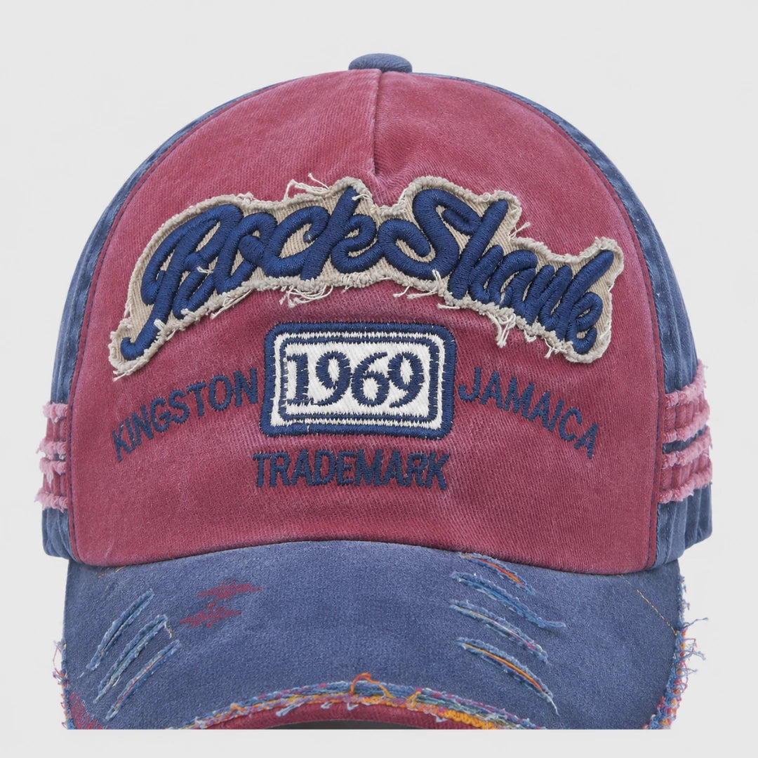 Josh & Tate - RockShank™ 1969 Baseball Cap - A distressed baseball cap with a dusty rose front panel and blue denim-like brim and side panels. The front features a large embroidered 'Rock n Roll' patch in blue with a beige outline, a central '1969' patch, and 'KINGSTON JAMAICA TRADEMARK' embroidered in blue.