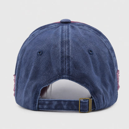 Josh & Tate - RockShank™ 1969 Baseball Cap - The back view of a washed blue denim baseball cap with a gold-tone metal buckle and pink fringe details on the sides, shown against a light gray background.