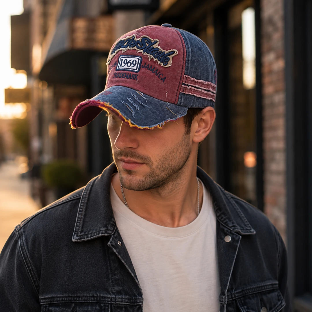 Josh & Tate - RockShank™ 1969 Baseball Cap - A man wearing a distressed baseball cap with a maroon and blue denim design, featuring embroidered text that reads 'Pistil Street' and '1969 Jamaica', photographed in an outdoor urban setting.