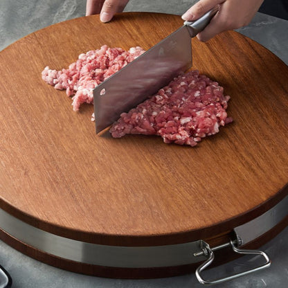 Person mincing meat on a wooden cutting board with a cleaver.