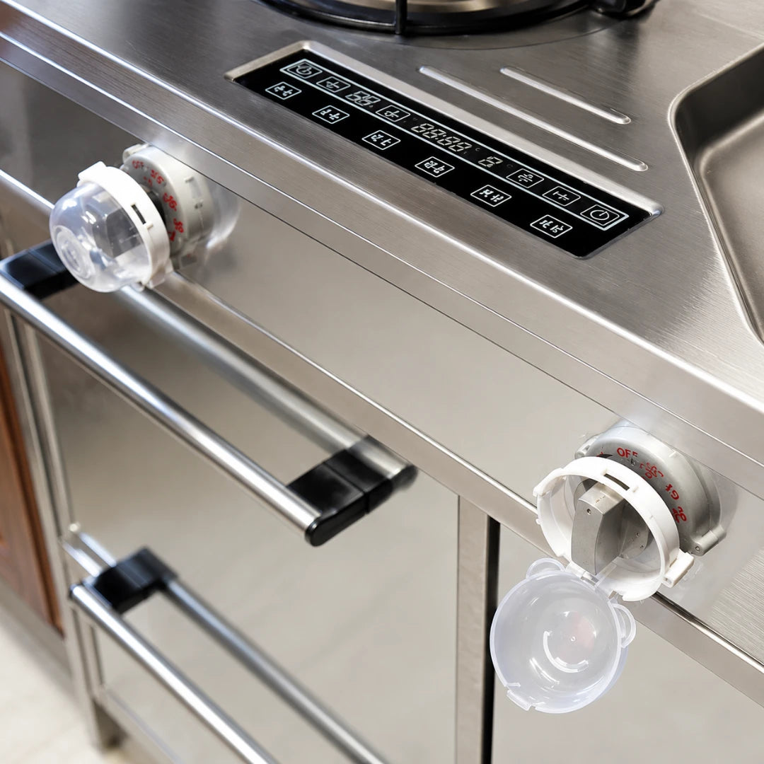 Josh & Tate - SafeKnob™ Child Safety Stove Covers - Close-up of a stainless steel kitchen appliance, likely a stove or oven control panel, with two clear plastic drip trays hanging below the knobs.