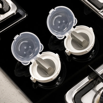 Josh & Tate - SafeKnob™ Child Safety Stove Covers - Two white and clear plastic kitchen drain stoppers with gray internal plugs, shown installed on a black glass stovetop.