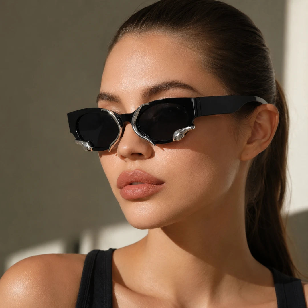 Josh & Tate - SerpentEdge™ Statement Sunglasses - A close-up of a woman wearing black cat-eye sunglasses with silver decorative accents on the temples, set against a warm, sunlit neutral background.