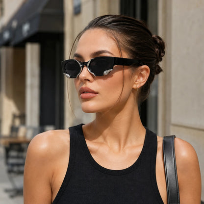 Josh & Tate - SerpentEdge™ Statement Sunglasses - A woman wearing black cat-eye sunglasses with silver mirrored temples, styled with a black ribbed tank top and a black shoulder bag strap, set against a blurred urban street background.