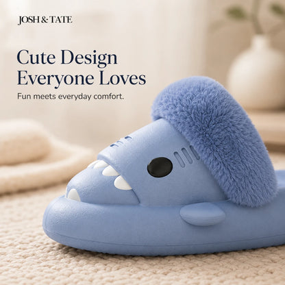 Josh & Tate - SharkStep™ Plush Slip-On Slipper - Blue shark-shaped slipper with fluffy details on a beige surface, featuring Josh & Tate branding.