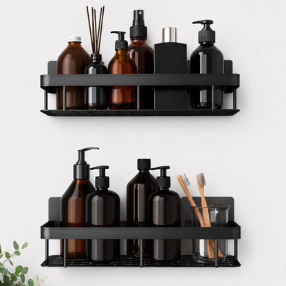 Josh & Tate - ShelfLoft™ Adhesive Shower Shelf - Two black metal wall-mounted bathroom shelves holding assorted toiletry bottles, a reed diffuser, a toothbrush holder with wooden toothbrushes, and a small plant sprig at the lower left, shown against a light gray wall.