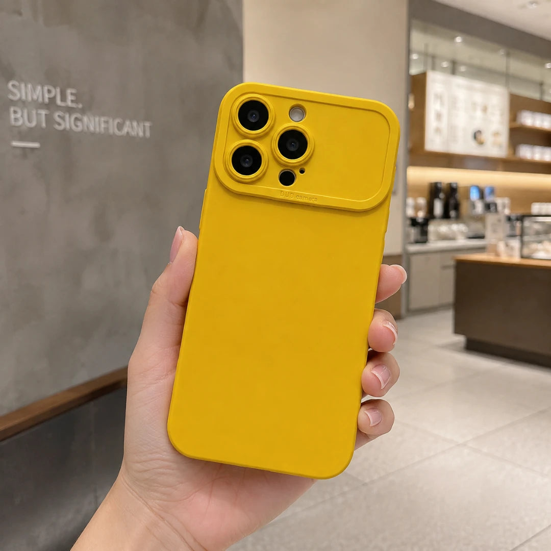 Josh & Tate - ShockProof™ iPhone Case - A hand holding a bright yellow phone case with a raised camera bumper, shown in a cafe setting.