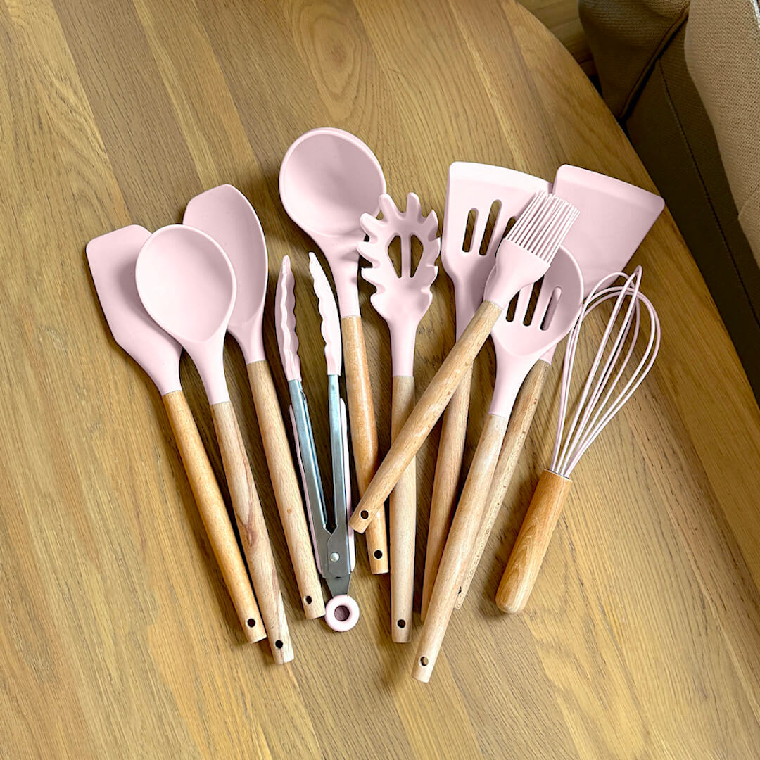 Set of pink and beige kitchen utensils on a wooden surface