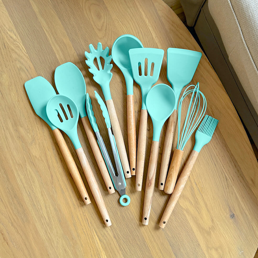 Set of turquoise silicone kitchen utensils with wooden handles on a wooden surface.