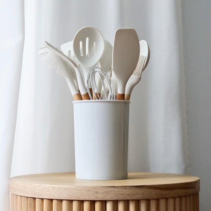 Set of kitchen utensils in a white container on a wooden surface with a light curtain background