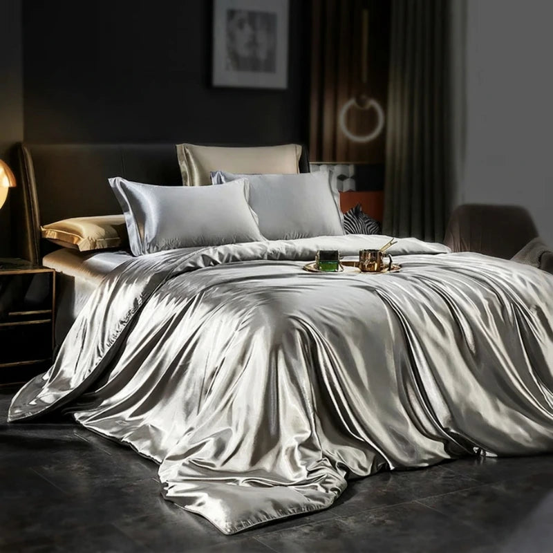 Silver satin bedding set on a bed in a dimly lit room.